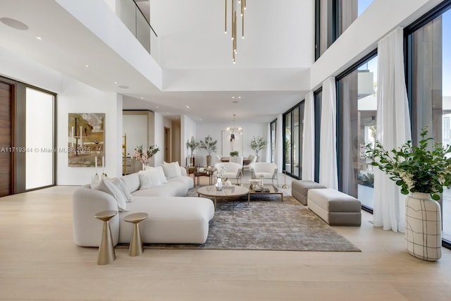 living room with a wealth of natural light, a chandelier, a high ceiling, and light hardwood / wood-style floors