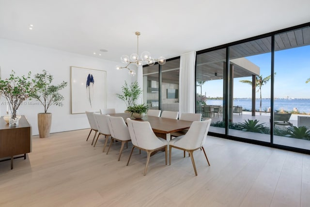 dining room with an inviting chandelier, a water view, light hardwood / wood-style flooring, and floor to ceiling windows