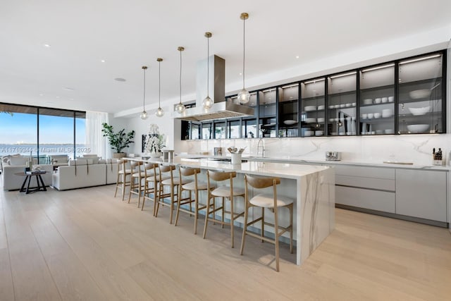 kitchen featuring a spacious island, island range hood, light hardwood / wood-style flooring, and hanging light fixtures