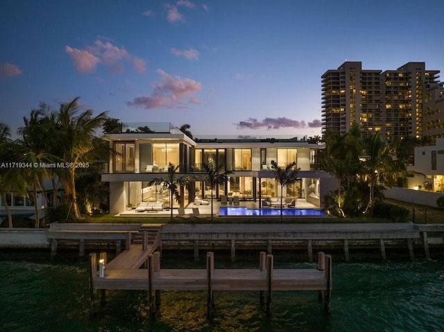 back house at dusk featuring solar panels, a water view, a swimming pool, a balcony, and a patio