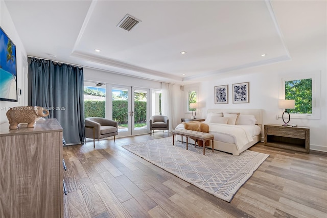 bedroom with french doors, a tray ceiling, light hardwood / wood-style floors, and access to exterior