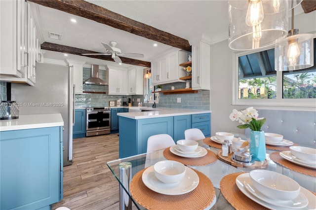 kitchen with white cabinets, blue cabinets, stainless steel range with electric cooktop, and wall chimney exhaust hood