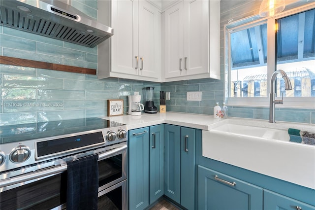 kitchen featuring stainless steel electric range, white cabinets, wall chimney range hood, sink, and tasteful backsplash