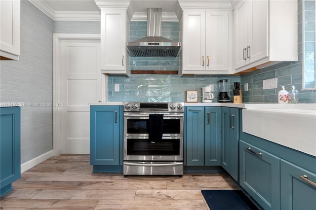 kitchen with white cabinets, wall chimney exhaust hood, range with two ovens, and ornamental molding