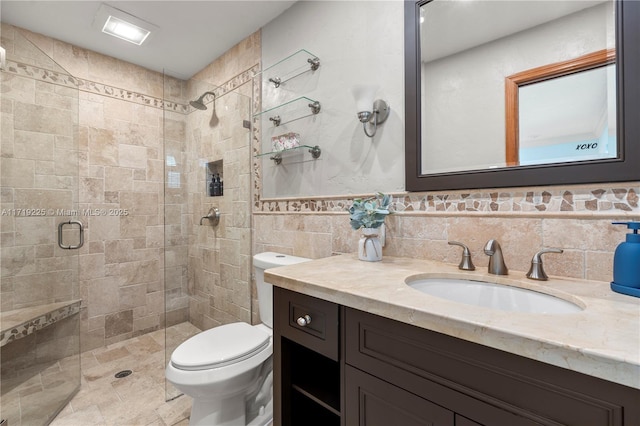 bathroom with a shower with door, vanity, tile walls, and toilet