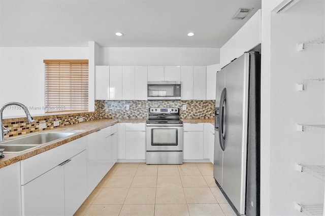 kitchen featuring white cabinets, sink, decorative backsplash, light tile patterned floors, and stainless steel appliances