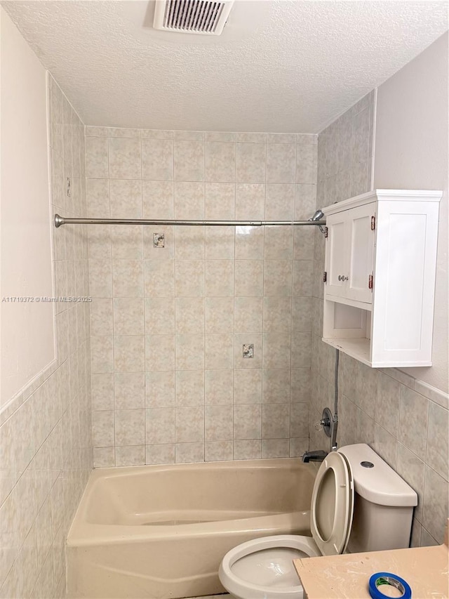 full bathroom with a textured ceiling, vanity, tiled shower / bath combo, tile walls, and toilet