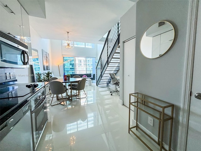 kitchen featuring appliances with stainless steel finishes, light tile patterned floors, a notable chandelier, white cabinetry, and hanging light fixtures