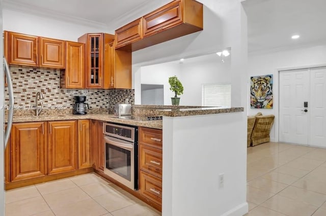 kitchen with backsplash, oven, crown molding, light tile patterned floors, and light stone counters