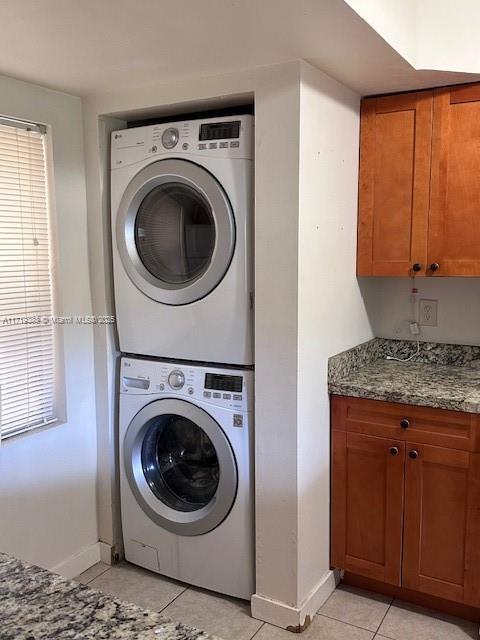 clothes washing area featuring light tile patterned floors, cabinets, and stacked washer / drying machine