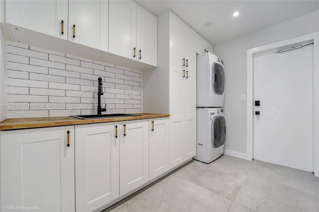 clothes washing area with sink, cabinets, and stacked washer and clothes dryer