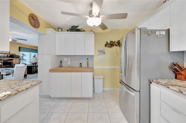 kitchen featuring stainless steel refrigerator, decorative backsplash, white cabinets, and light stone countertops