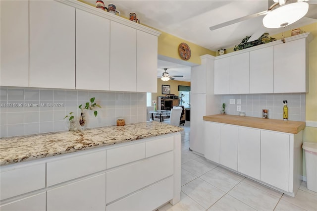 kitchen with backsplash, white cabinetry, light tile patterned floors, and light stone counters