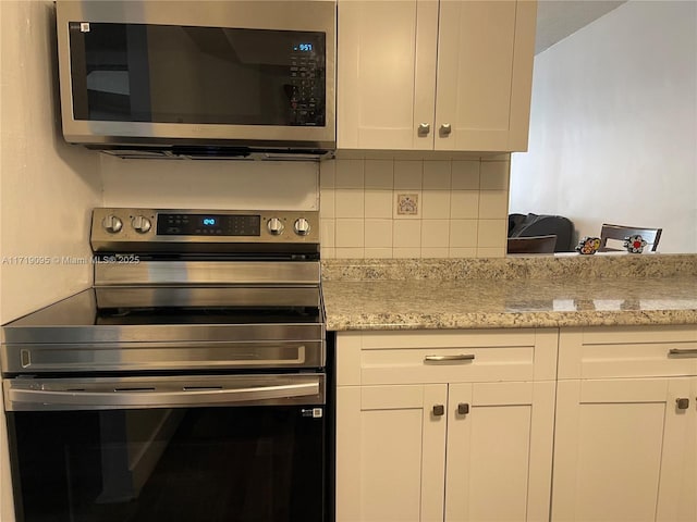 kitchen with white cabinets, backsplash, light stone countertops, and stainless steel appliances