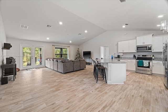 kitchen with appliances with stainless steel finishes, a kitchen breakfast bar, a center island with sink, light hardwood / wood-style flooring, and white cabinets