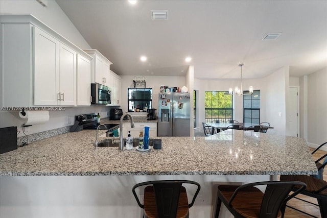 kitchen with appliances with stainless steel finishes, a notable chandelier, white cabinetry, hanging light fixtures, and a breakfast bar area