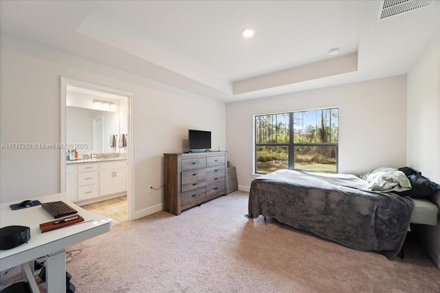 carpeted bedroom with a tray ceiling and ensuite bathroom