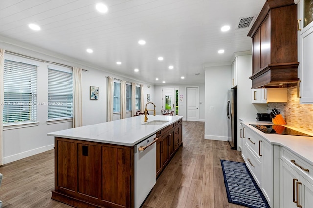 kitchen with dishwashing machine, a kitchen island with sink, sink, white cabinets, and light hardwood / wood-style floors