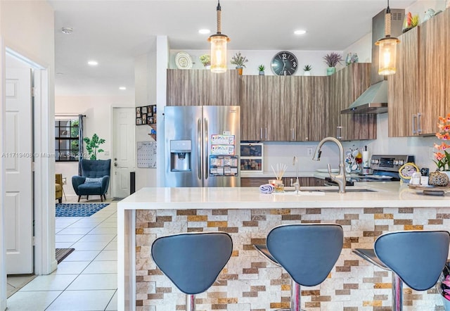 kitchen with kitchen peninsula, appliances with stainless steel finishes, wall chimney exhaust hood, a breakfast bar, and pendant lighting