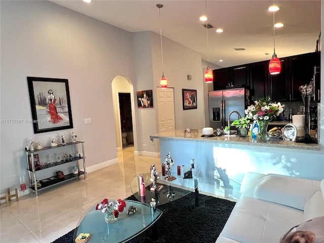 kitchen featuring hanging light fixtures, stainless steel fridge with ice dispenser, light tile patterned flooring, light stone counters, and kitchen peninsula