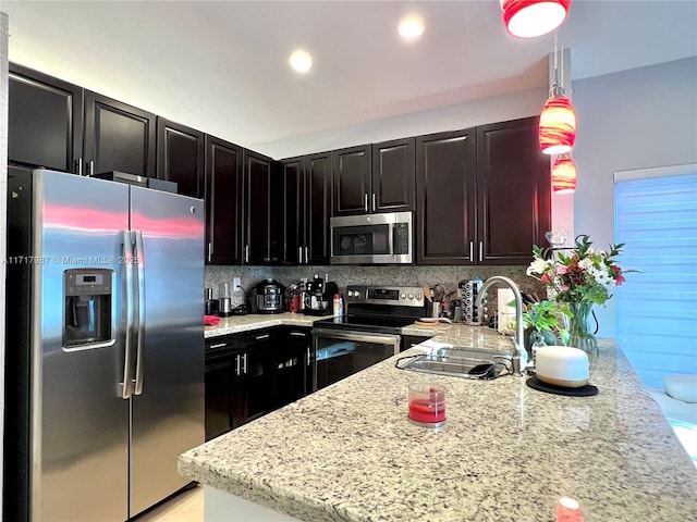 kitchen with light stone countertops, tasteful backsplash, stainless steel appliances, sink, and pendant lighting