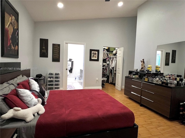 bedroom with light hardwood / wood-style floors, a walk in closet, a closet, and vaulted ceiling