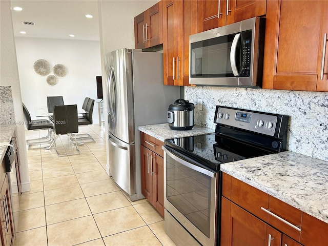 kitchen with backsplash, light stone counters, and stainless steel appliances