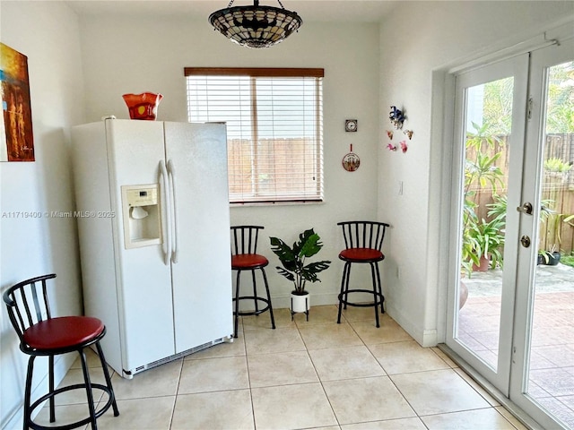 kitchen featuring a kitchen bar, white fridge with ice dispenser, light tile patterned floors, and french doors