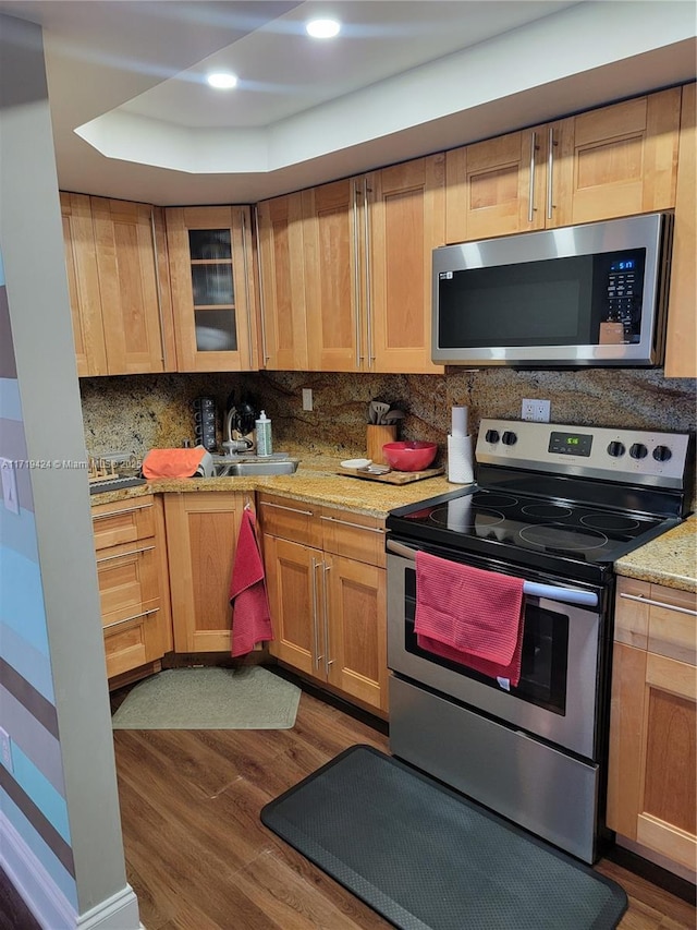 kitchen featuring appliances with stainless steel finishes, backsplash, light stone counters, a tray ceiling, and dark hardwood / wood-style flooring