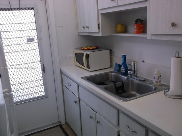 kitchen with white microwave, a sink, white cabinetry, light countertops, and open shelves