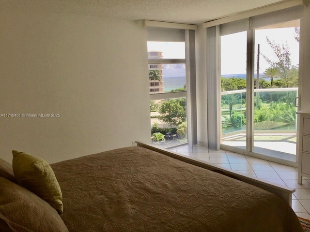 unfurnished bedroom with tile patterned floors, floor to ceiling windows, a textured ceiling, access to outside, and a water view