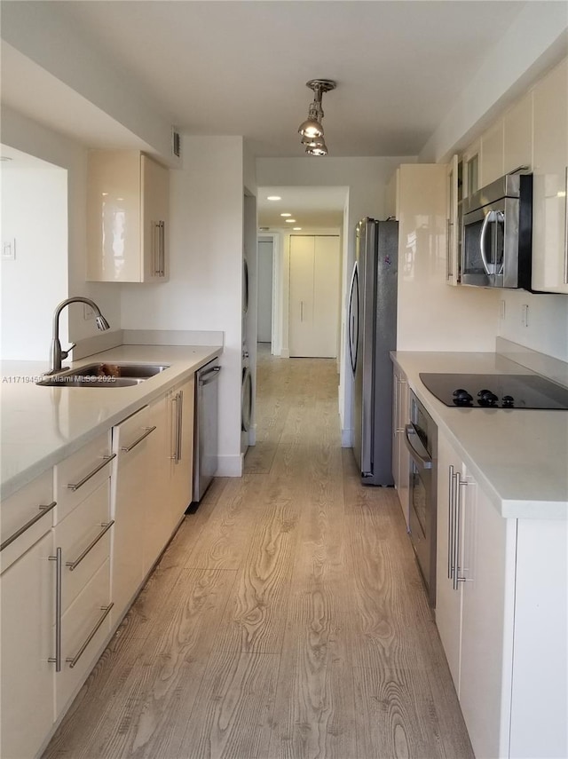 kitchen with stacked washing maching and dryer, light wood-type flooring, sink, and appliances with stainless steel finishes