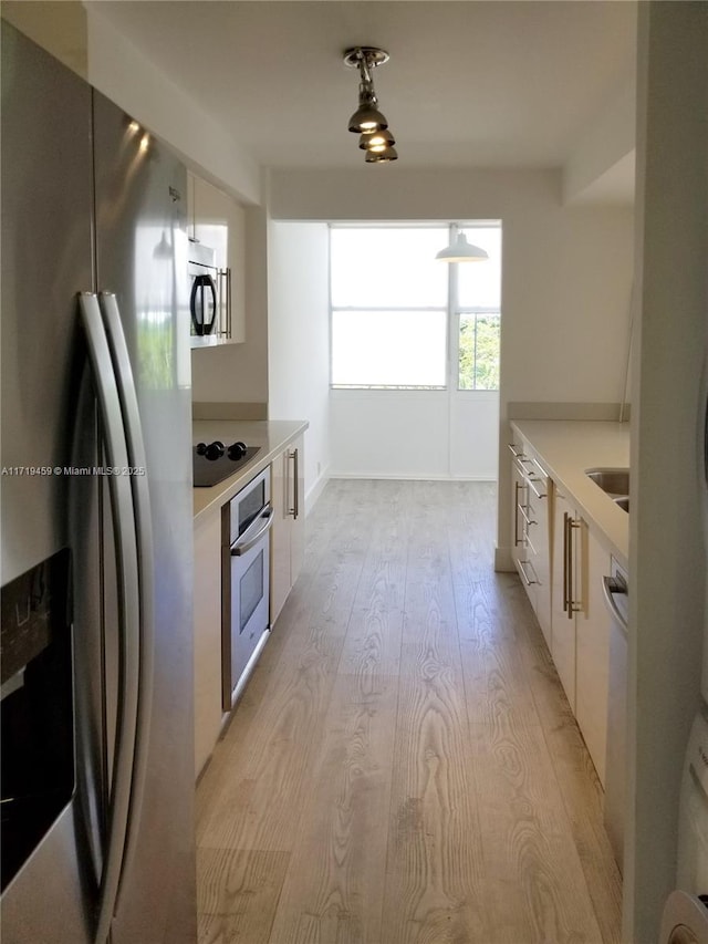 kitchen with white cabinets, appliances with stainless steel finishes, light wood-type flooring, and sink