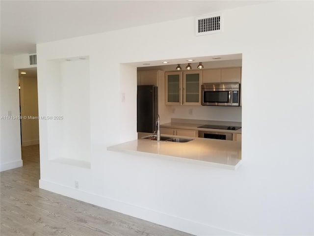 kitchen with stovetop, light hardwood / wood-style floors, black fridge, and sink