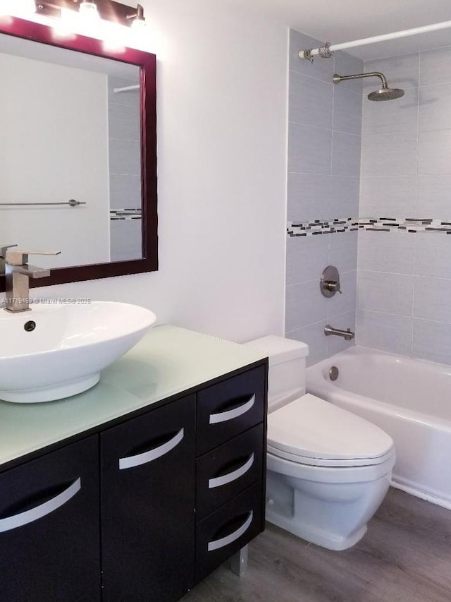 full bathroom with tiled shower / bath combo, toilet, wood-type flooring, and vanity