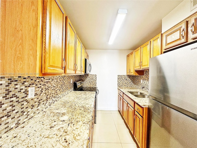 kitchen featuring light stone countertops, sink, backsplash, light tile patterned flooring, and appliances with stainless steel finishes