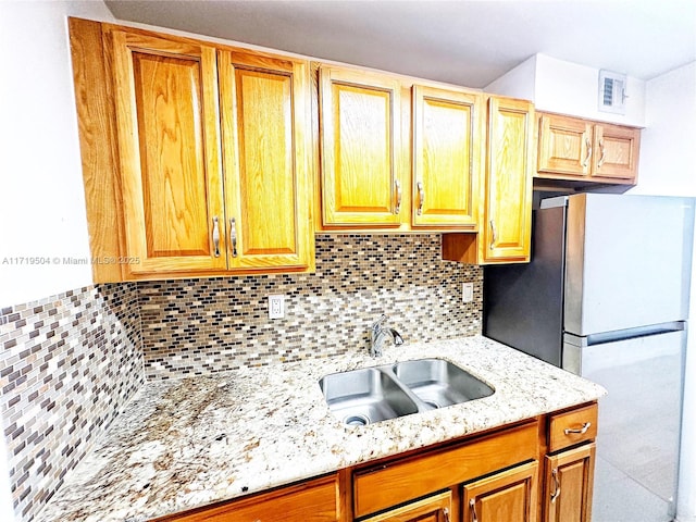 kitchen with stainless steel fridge, light stone countertops, sink, and tasteful backsplash