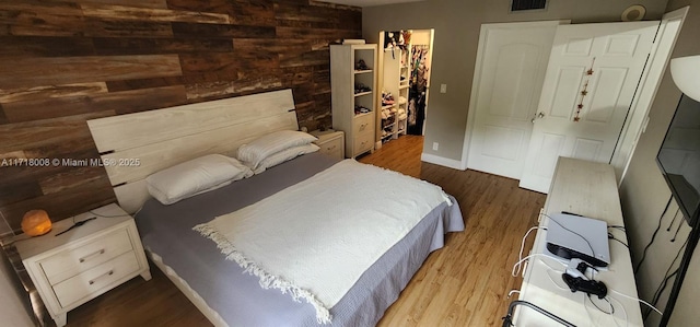 bedroom with hardwood / wood-style flooring, wood walls, a spacious closet, and a closet