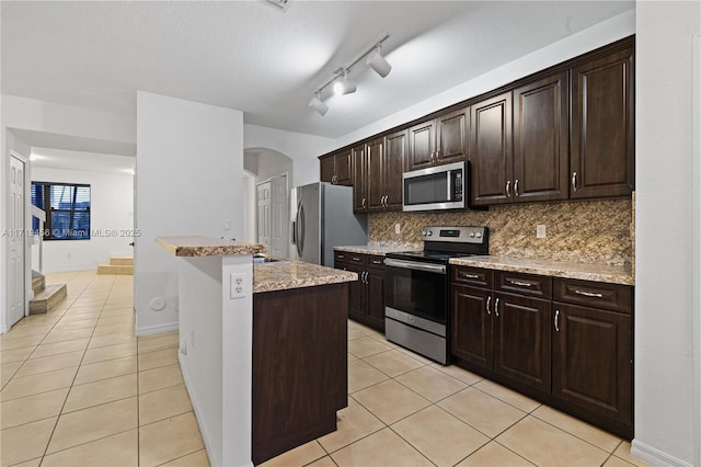 kitchen featuring appliances with stainless steel finishes, tasteful backsplash, dark brown cabinets, a center island, and light tile patterned flooring