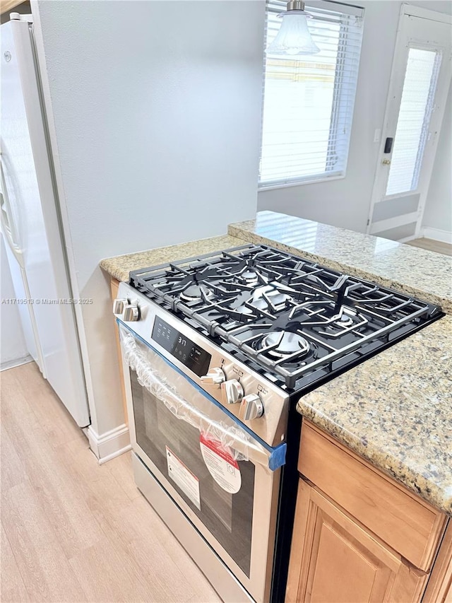 kitchen featuring light stone countertops, light brown cabinetry, stainless steel stove, and light hardwood / wood-style floors