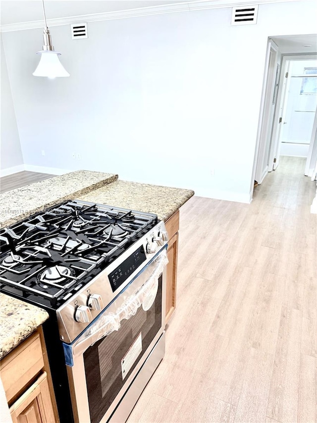 kitchen featuring stainless steel gas stove, light hardwood / wood-style floors, light stone countertops, and hanging light fixtures