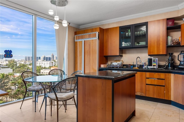 kitchen featuring hanging light fixtures, crown molding, dark stone countertops, and paneled built in fridge