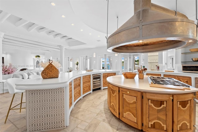 kitchen with decorative columns, decorative light fixtures, a center island, wine cooler, and stainless steel gas stovetop