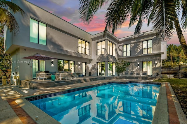 pool at dusk with outdoor lounge area and a patio area