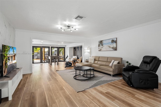 living room with a textured ceiling, an inviting chandelier, light hardwood / wood-style floors, and french doors