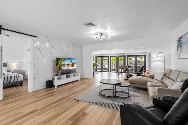 living room with a textured ceiling, ornamental molding, light hardwood / wood-style floors, and french doors