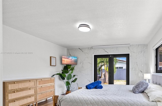 bedroom with access to exterior, french doors, a textured ceiling, and hardwood / wood-style floors