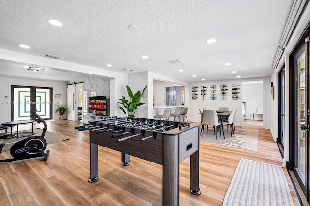 game room featuring a barn door, a textured ceiling, and light hardwood / wood-style floors