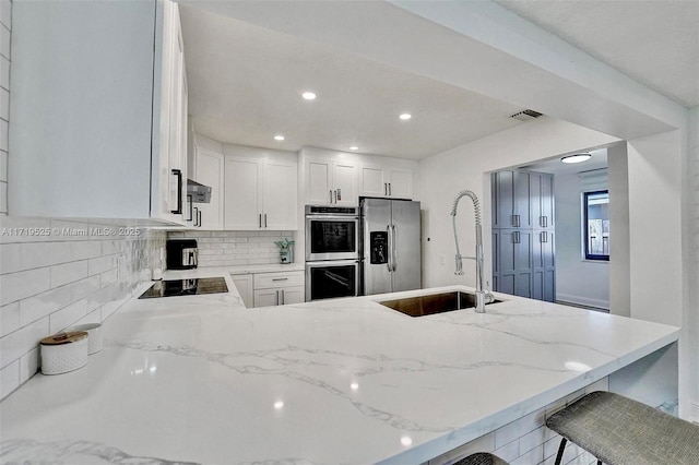 kitchen with a kitchen bar, sink, white cabinetry, stainless steel appliances, and light stone counters