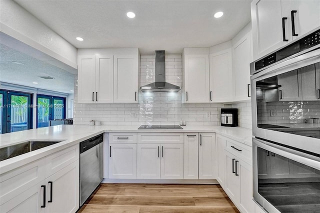 kitchen featuring decorative backsplash, white cabinets, wall chimney exhaust hood, and stainless steel appliances